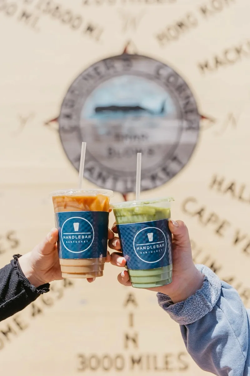 Two guests raising Handlebar Nantucket cups in front of a Nantucket compass rose mural