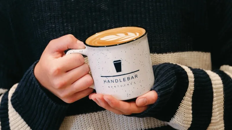 Hands holding a Handlebar branded mug with latte art